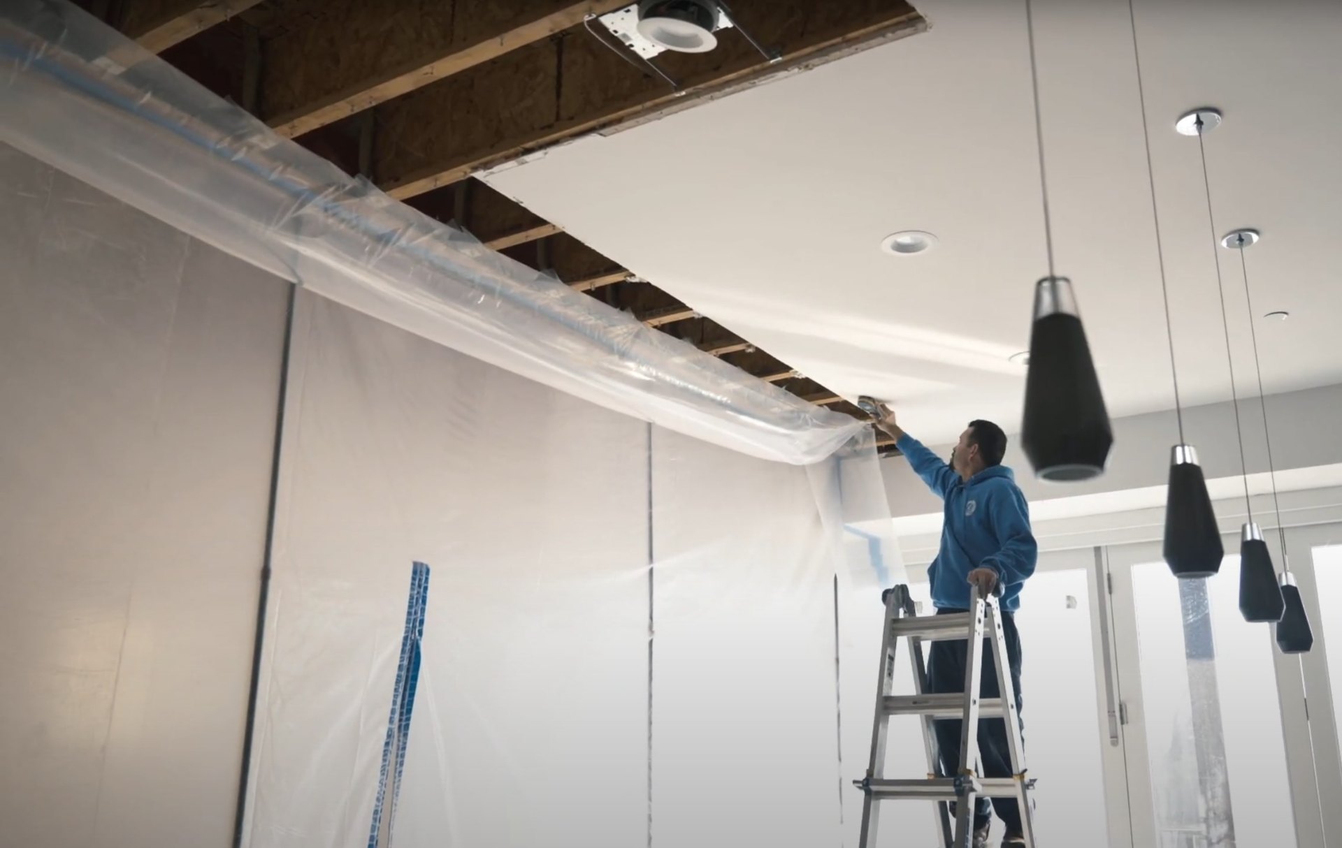 Commercial water damage restoration work - ceiling repair and protection in Midlothian business Water damage restoration professional on ladder working on ceiling repair with protective plastic sheeting